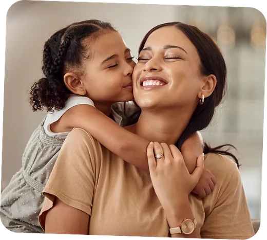 Mãe sorrindo enquanto a filha pequena a abraça e beija o rosto